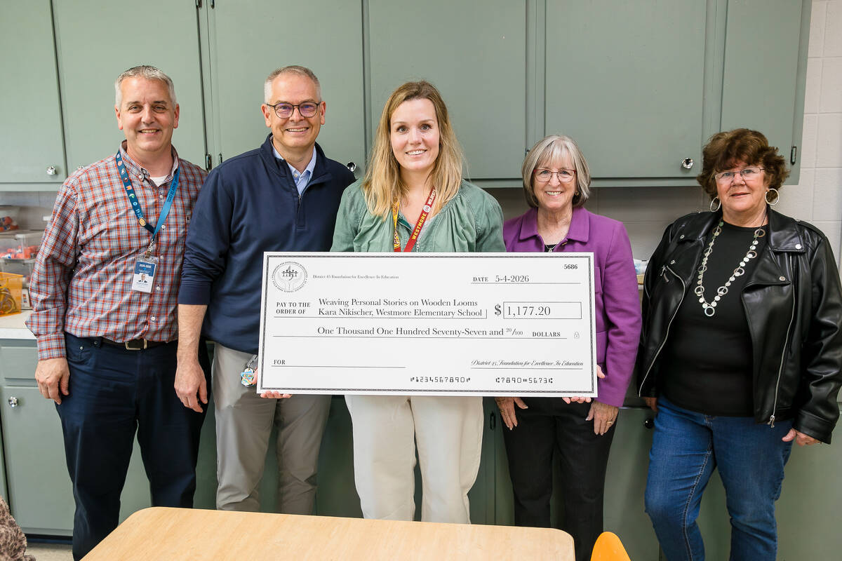 Five adults stand indoors, smiling at the camera. The woman in the middle holds a large ceremonial check for $1,177.20 made out to Windsor Elementary School. The group appears to be celebrating the donation.