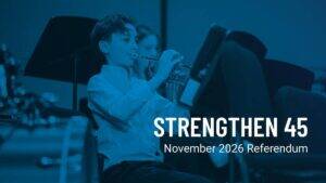 A boy in a white shirt plays the trumpet in a band. Text reads STRENGTHEN 45 November 2026 Referendum..